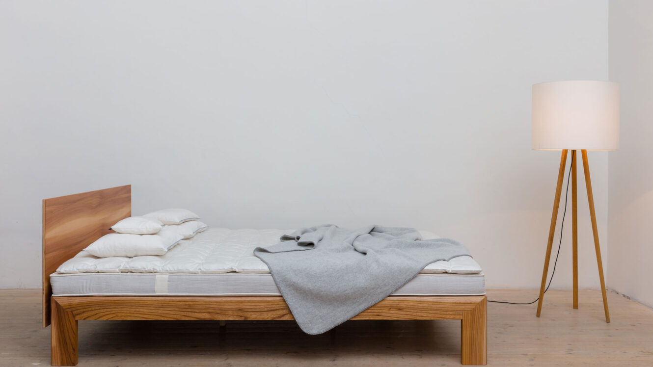 Das Bett seitlich mit einem angestecktem Kopfhaupt vor einer weißen Wand.